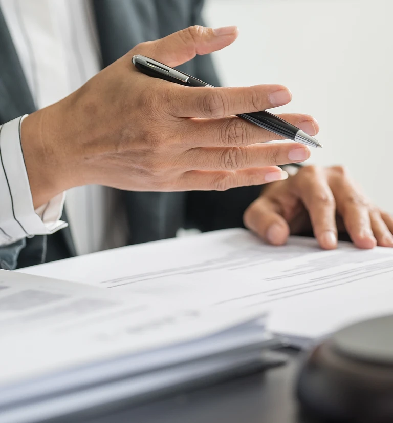 Close-up of a person holding a black pen and reviewing documents on a desk.