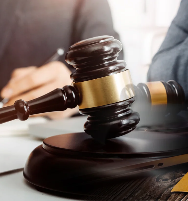 Close-up of a dark wooden judge's gavel with gold band striking a sound block on a desk.