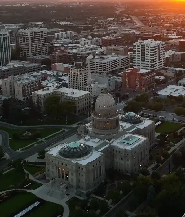 Aerial view of a cityscape at sunset featuring a domed capitol building and surrounding urban structures.