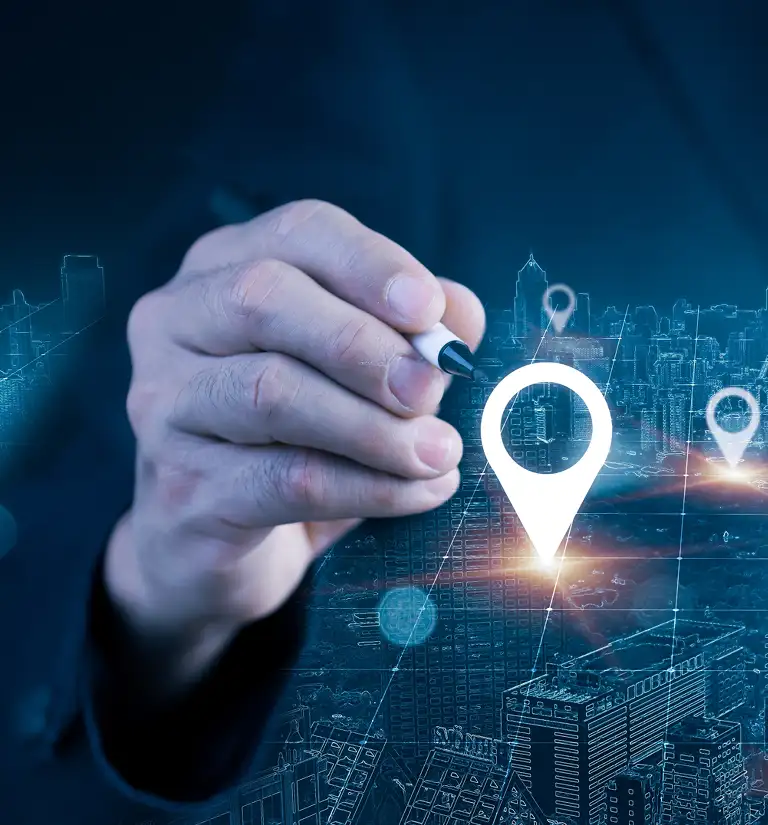 Hand holding a pen pointing at digital location markers over a cityscape background.