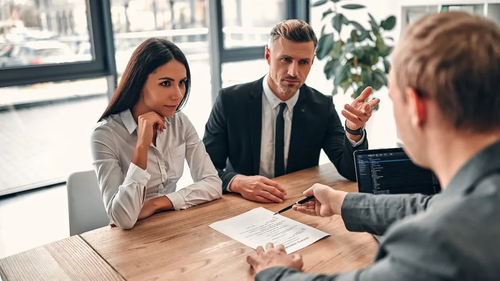 Three professionals engaged in a business discussion around a wooden table with a document and laptop.