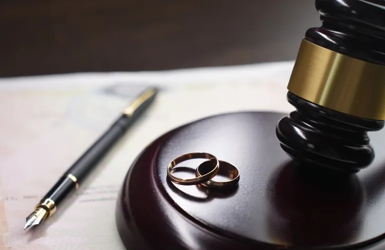 Close-up of two gold wedding rings on a wooden judge's gavel base with a fountain pen on a document.