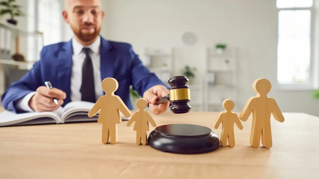 Man in blue suit holding judge’s gavel over wooden family figures on desk.