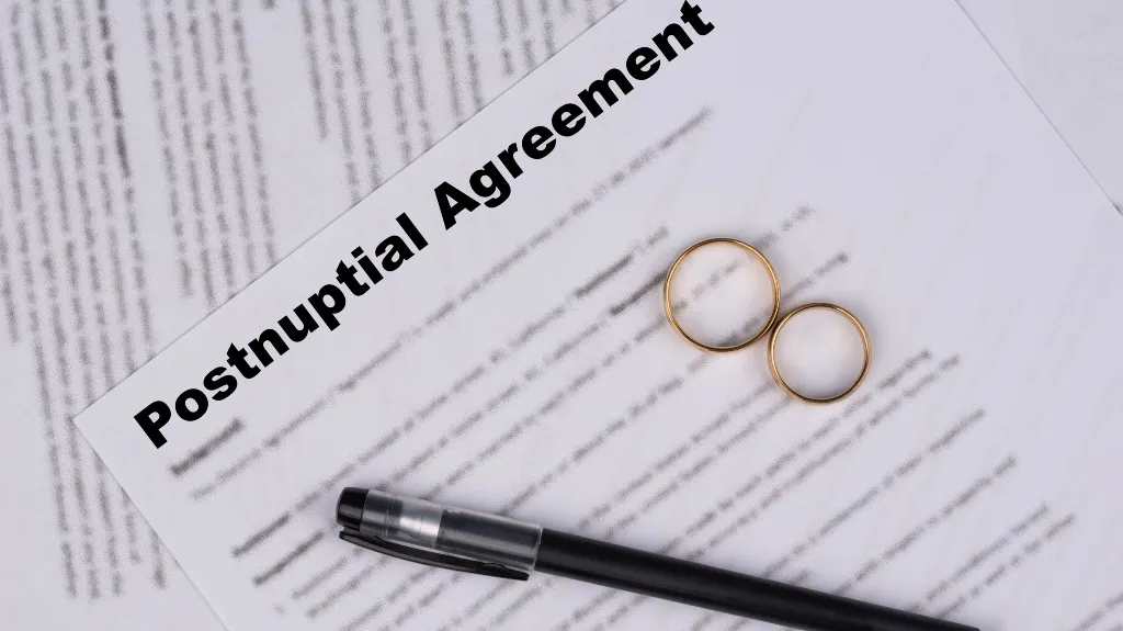 Postnuptial agreement document with two gold wedding rings and a black pen on top.
