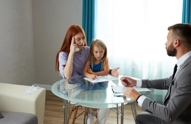 A concerned woman and young girl sitting at a glass table with a man in a suit during a consultation.