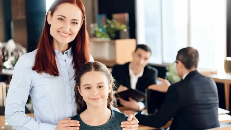 Smiling woman with red hair and young girl in foreground, two men in suits conversing in background.
