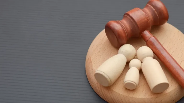 Wooden judge's gavel resting on a round wooden base with four beige wooden figurines.