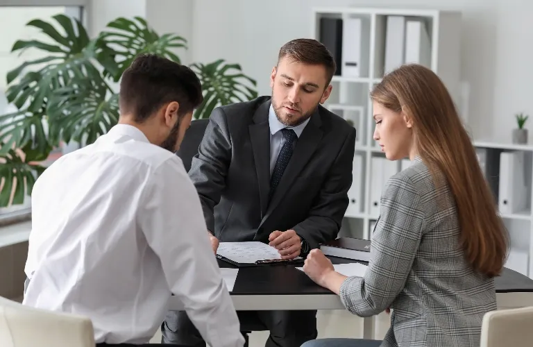 Three business professionals, two men and one woman, engaged in a discussion over documents at an office desk.