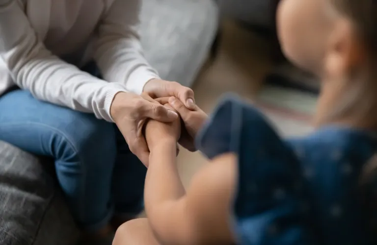 Adult and child holding hands in a comforting gesture, indoor setting.