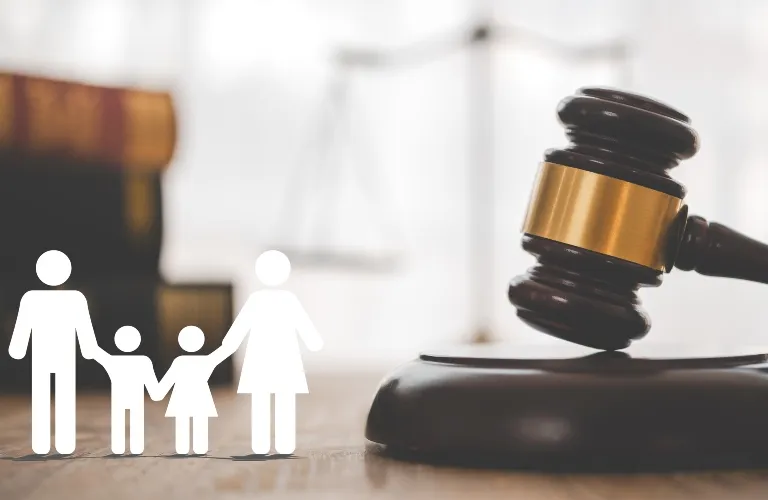 Wooden judge's gavel on sound block with white family icons and blurred scales of justice background.