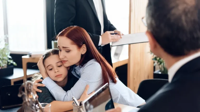 Woman with red hair comforting a young girl in an office setting with two men in suits.