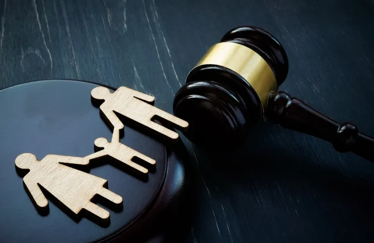 Wooden cutouts of a family on a judge's gavel and sound block on dark surface.
