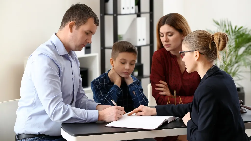 Professional woman in glasses explaining documents to a man, woman, and child at office.