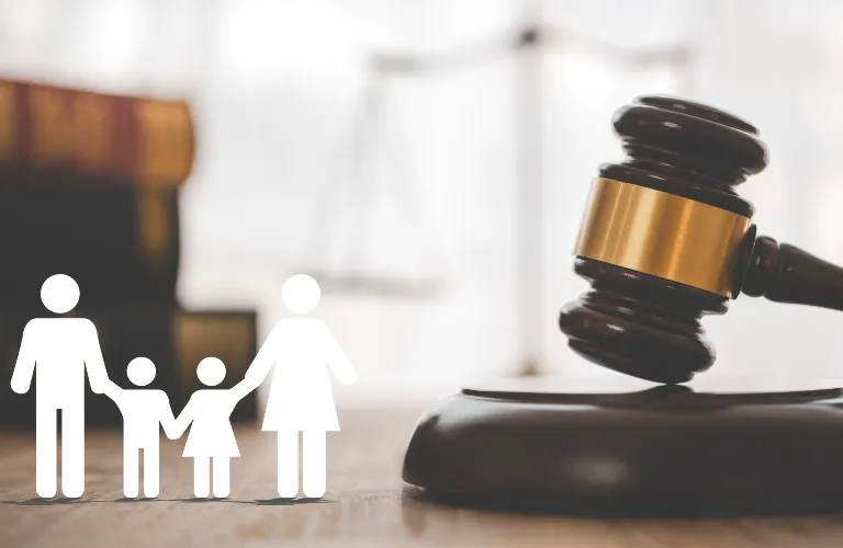 Wooden judge's gavel with brass band beside white family icon and blurred law books background.