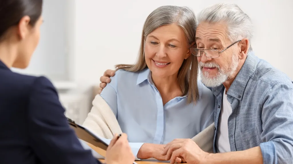 Elderly couple smiling and discussing documents with a professional in an office setting.