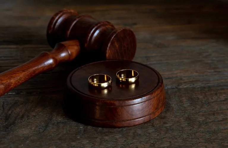 Wooden judge's gavel and block with two gold wedding rings on top, placed on dark wooden surface.