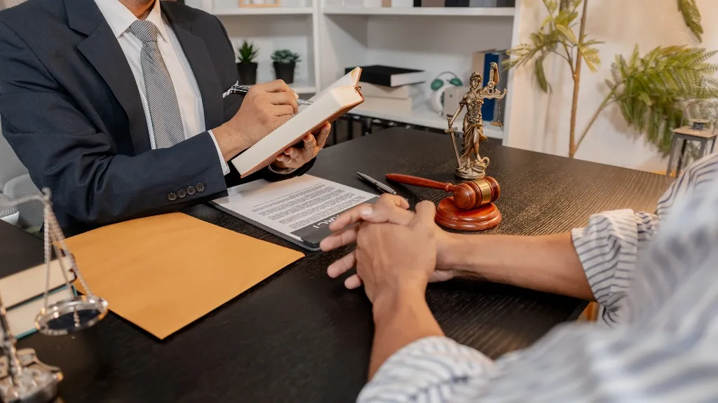 Professional consultation scene with lawyer in suit taking notes, client seated across desk.
